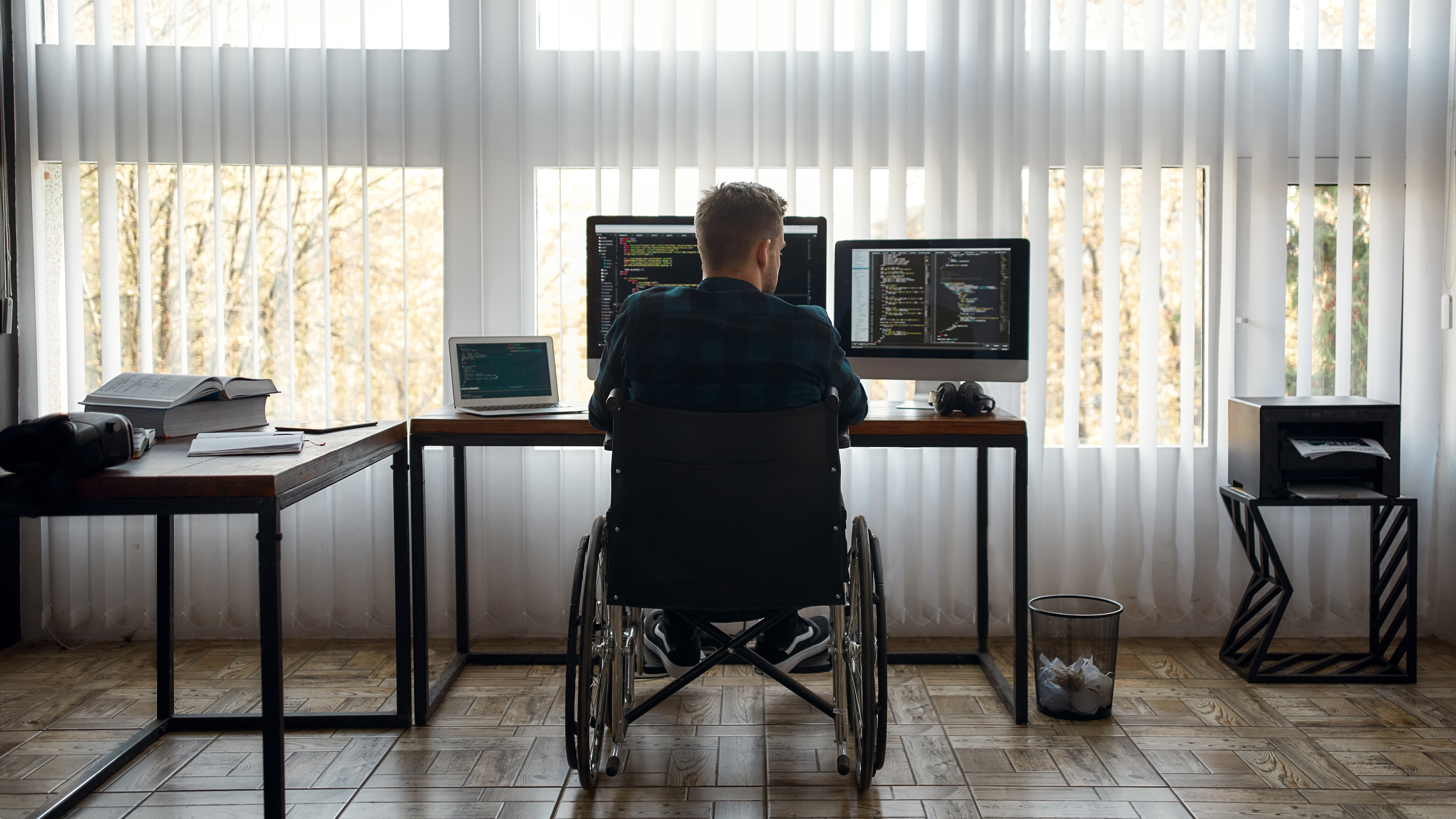 Persona en silla de ruedas trabajando delante de dos pantallas de ordenador