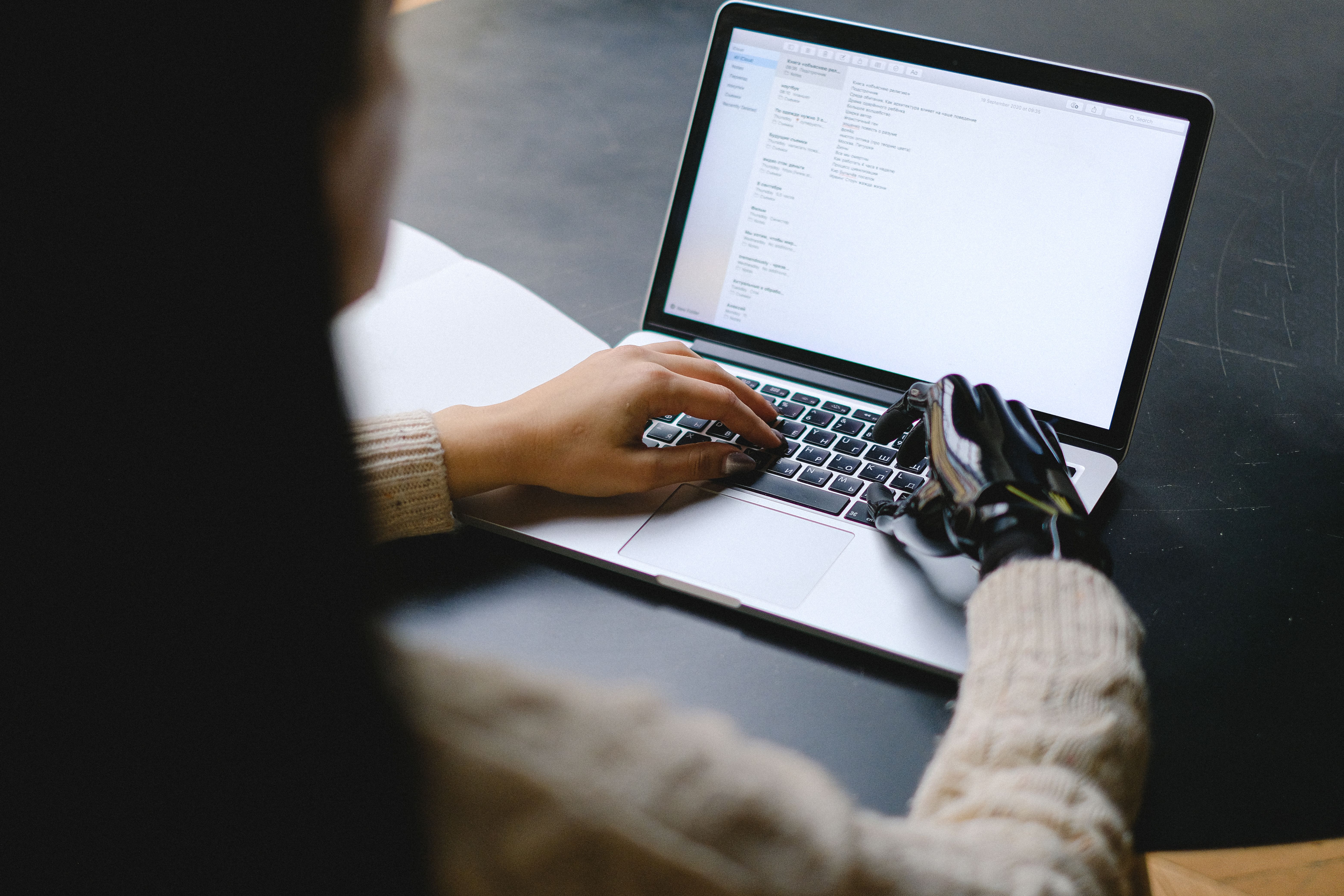 Persona usando un portátil, con una mano y una prótesis robótica escribiendo en el teclado.