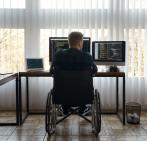 Persona en silla de ruedas trabajando delante de dos pantallas de ordenador
