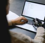 Persona usando un portátil, con una mano y una prótesis robótica escribiendo en el teclado.