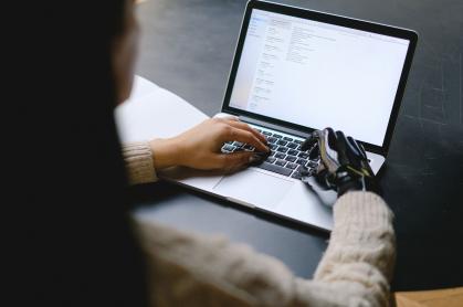 Persona usando un portátil, con una mano y una prótesis robótica escribiendo en el teclado.